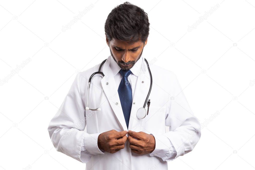 Male indian medic buttoningwhite medical coat while looking isolated on studio background