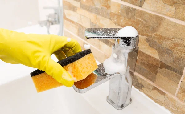 人清洁水龙头用橙色海绵和泡沫戴黄色卫生手套 — 图库照片