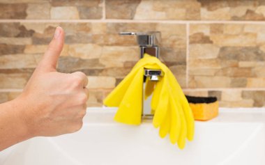 Jest olarak yukarı onaylaması sarı eldivenler ve sünger ile temiz lavabo önünde kavramı