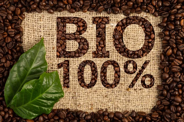 Advertisement for hundred percent bio coffee written with roasted beans on burlap bag background