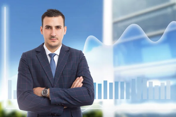 Broker man with crossed arms and serious expression standing in front of growing graph on building background