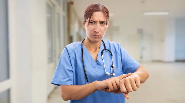 Angry nurse woman pointing at wrist with index finger as late for work concept