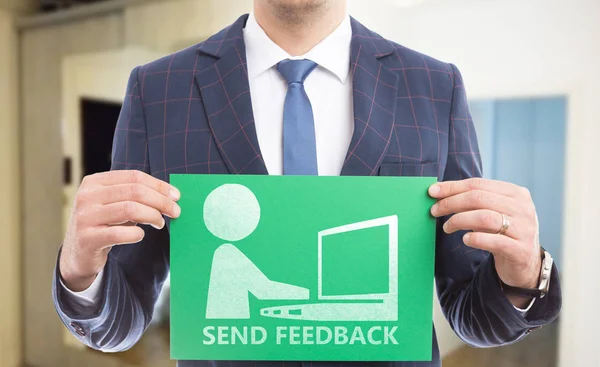 Man holding green paper with send feedback text and drawing of person writing on laptop