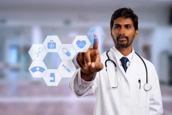 Male indian physician touching health care text button on futuristic screen with symbols as medical technology concept