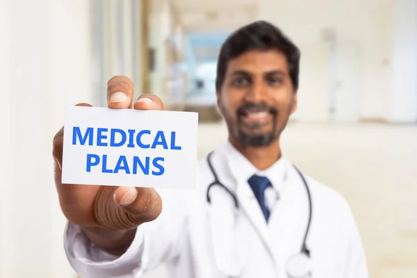 Médico segurando cartão planos médicos em han — Fotografia de Stock