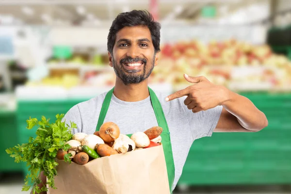 Employé de l'hypermarché pointant vers sac avec légumes — Photo