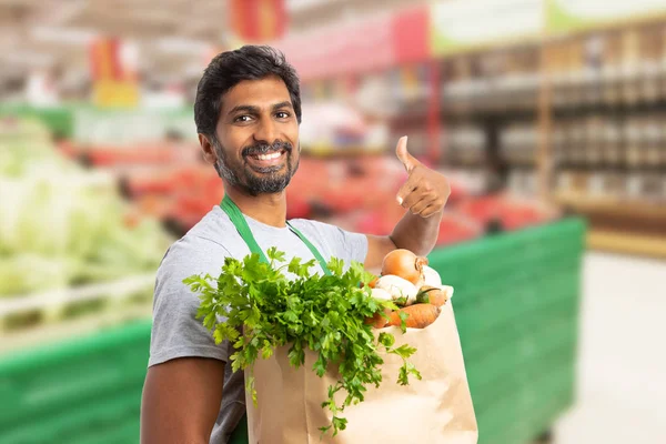 Worker at grocery store holding vegetable ba