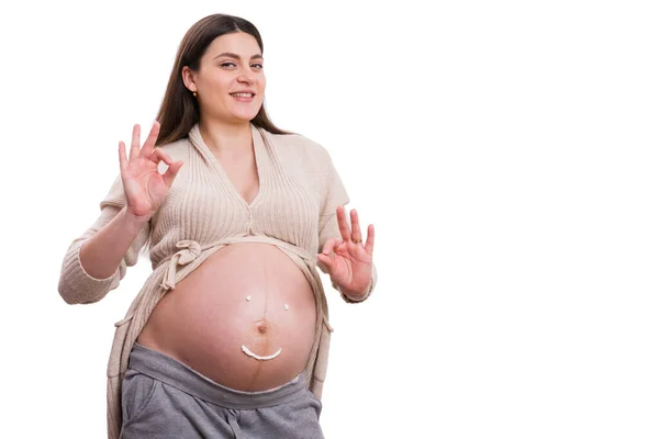 幸せな妊娠中の女性とともにクリームスマイリー顔描画上のおなか作り大丈夫ジェスチャーとともに手孤立上の白い背景として完璧な妊娠コンセプト — ストック写真