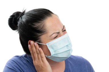 Yetişkin kadın modeli, beyaz stüdyo arka planındaki kirlenmeden korunmak için cerrahi tek kullanımlık maske takan 19 grip salgını semptomunu bastırdığı için el kulağına dokunuyor.