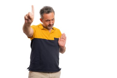 Ciddi bir ifadeye sahip öfkeli yetişkin bir adam beyaz stüdyo arka planında izole edilmiş günlük tişört giyerek işaret parmağı ve avuç içi jesti yapıyor.