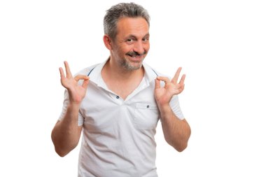 Neşeli yetişkin erkek mankeni polo tişört tasmasını sunuyor. Stüdyo arka planında izole edilmiş moda yaz kıyafetleri konsepti olarak parmaklarını kullanıyor.