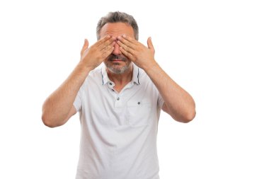 Erkek model gözleri kapatıyor. Gözleri görmüyor. Gizli bir konsept değil. Beyaz stüdyo arka planında izole edilmiş şık bir tişört giyiyor.