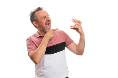 Korkak suratı olan yetişkin bir adam beyaz stüdyo arka planında izole edilmiş takma diş protezini işaret ediyor gibi bağırıyor.