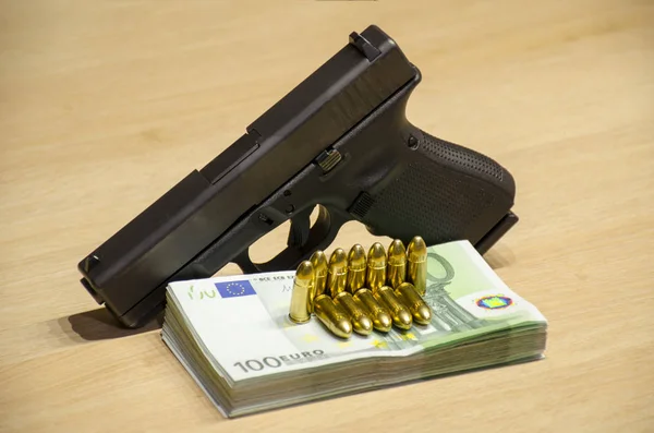 The pistol with bullets stays behind money with bllured wall backspace.