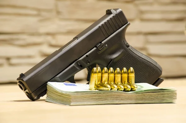 The pistol with bullets stays behind money with bllured wall backspace.