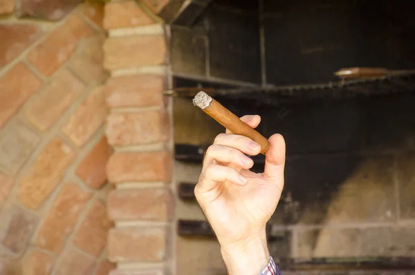 一个男人的手拿着一个模糊的砖墙前的古巴雪茄 — 图库照片