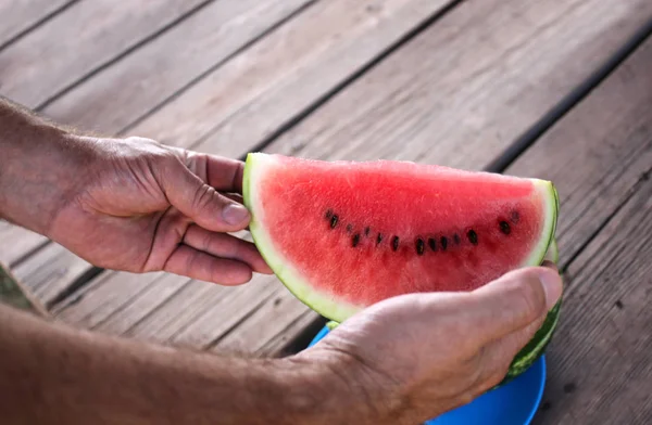 Closeup picture of a watermelon and man\'s hands on a wooden surface