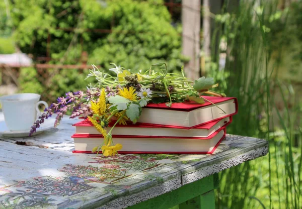 Still life in a rural garden with books, wild flowers, a jug and a cup of coffee on a vintage table