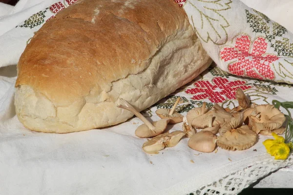 Picture of a loaf of handmade bread in a flowered cloth and pile of mushrooms next to it