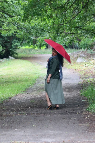 緑のスカートを着た若い美しい女性と赤い傘を持って公園を歩く緑のシャツ — ストック写真