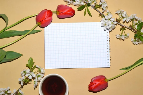 Open Notepad for writing framed with tulips and white flowers, and a Cup of tea.