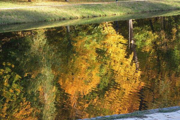 Bright autumn landscape - red, yellow and green trees on the shore of the lake are reflected in the water. Abstract autumnal background. Colorful autumn. Sunny day.