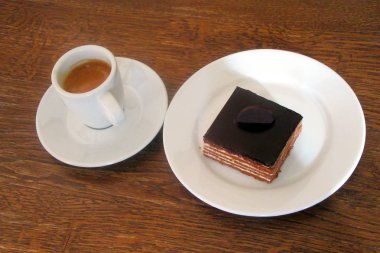 Siyah kahve bir fincan ve yanında bir plaka üzerinde bir çikolata peynirli kekim. Kahverengi ahşap zemin.