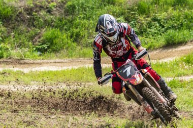 Motocross. Motosikletçi toprak bir yol boyunca koşar, toprak tekerleklerin altından uçar. Parlak bahar yeşilliklerinin arka planında. Close. Aktif aşırı dinlenme.