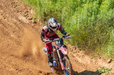 Motocross. Motosikletçi toprak bir yolda koşar, tekerleklerin altından toz uçar. Aktif aşırı dinlenme.