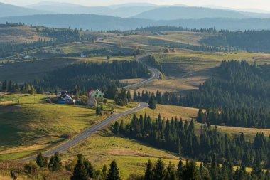Dağın eteklerinde dolambaçlı uzun bir yol. Birkaç küçük ev. Arka planda yüksek dağlar var. Sonbahar manzarası. Panoramik görünüm.