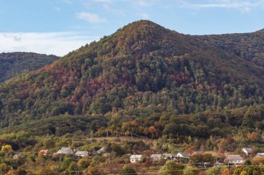 Yüksek dağlar ve mavi bulutlu gökyüzü. Birkaç küçük ev. Sonbahar manzarası. Panoramik görünüm.