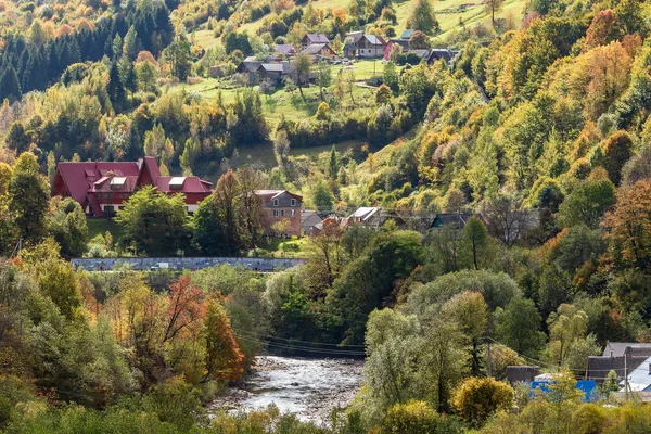 Nehir kıyısındaki dağların yamaçlarında küçük bir dağ köyü. Sonbahar manzarası. Panoramik görünüm.