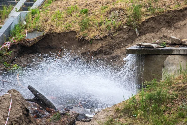 Accident sewerage system. Water supply failure. Breakthrough of the water supply system. A fountain of water flows out of the sewer under high pressure. Wet soil. Kyiv. Ukraine.