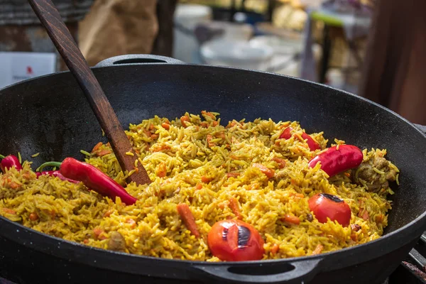 Healthy street food to go - in a large cauldron hot pilaf with pieces of meat and whole hot red pepper. Delicious food cooked over an open fire, which is offered at a street food fair, event, festival.