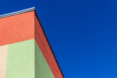 Parlak mavi gökyüzü ile birleştirilmiş yeşil ve turuncu bir binanın soyut bir parçası. Soyut kentsel mimari arkaplan. 