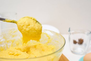 Pirinç unundan, tereyağından, yumurtadan, şekerden yapılan keklerin hamuru kaşıktan akıyor. Hamur dokusunun şeffaf bir tabakta yakın plan görüntüsü.