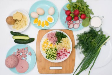Adım adım Rus soğuk okroshka çorbası tarifi ev yapımı okroshka sosisi, sebze, yumurta, salatalık, patates, turp malzemeleri. Işık arkaplan üzerindeki üst görünüm.