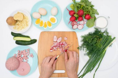 Adım adım Rus soğuk okroshka çorbası tarifi, ev yapımı okroshka malzemeleri bıçak sosisi, otlar, yumurtalar, salatalık, patates, turp. Işık arkaplan üzerindeki üst görünüm.