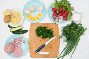 Adım adım Rus soğuk okroshka çorbası tarifi, ev yapımı okroshka malzemeleri bıçak sosisi, otlar, yumurtalar, salatalık, patates, turp. Işık arkaplan üzerindeki üst görünüm.