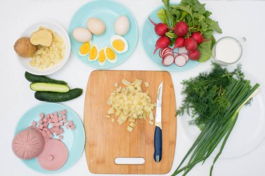 Adım adım Rus soğuk okroshka çorbası tarifi, ev yapımı okroshka malzemeleri bıçak sosisi, otlar, yumurtalar, salatalık, patates, turp. Işık arkaplan üzerindeki üst görünüm.