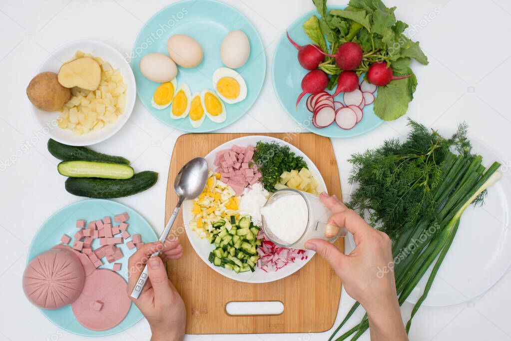 step by step recipe for Russian cold okroshka soup, ingredients for homemade okroshka-sausage, greens, eggs, cucumbers, potatoes, radishes. top view on a light background.