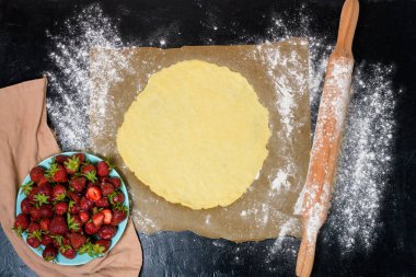 Adım adım tarif evde çilek ile galetta yapma süreci, koyu arkaplanda üst görünüm, çilekli turta malzemeleri.