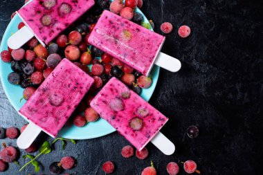 Doğal organik şerbet. Dört tane dondurma, siyah frenk üzümü ve kırmızı böğürtlen. Yazın soğuk süt meyveli tatlı. Koyu arkaplanda en üstteki görünüm.