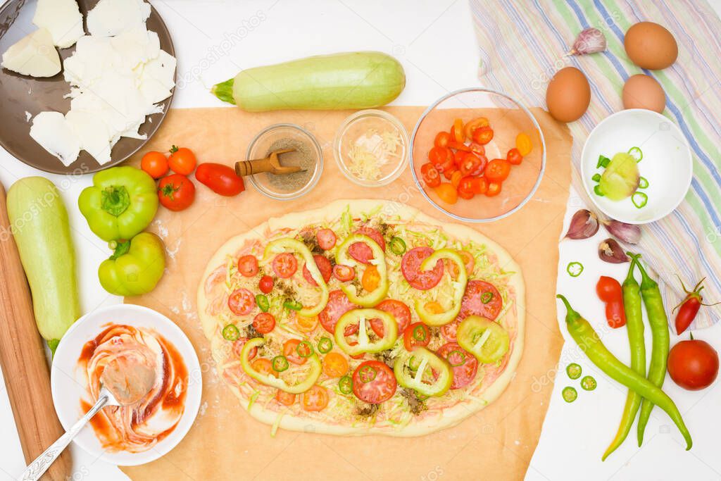step by step recipe for cooking homemade vegan pizza with zucchini, tomatoes, peppers, mozzarella . hands of a woman preparing a pizza from the top view . light background.