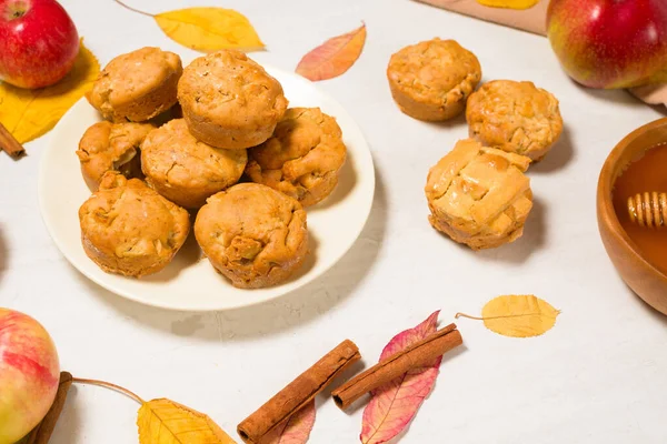 Mevsimlik elma ve tarçınlı bal ile sonbahar pişirme konsepti. Elmalı çörekler ve kekler, sonbahar sarısı yapraklı açık bir arka planda bir tabağın üstünde.