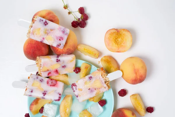 fresh summer ice cream on a stick with peach and raspberry berries . on light background.