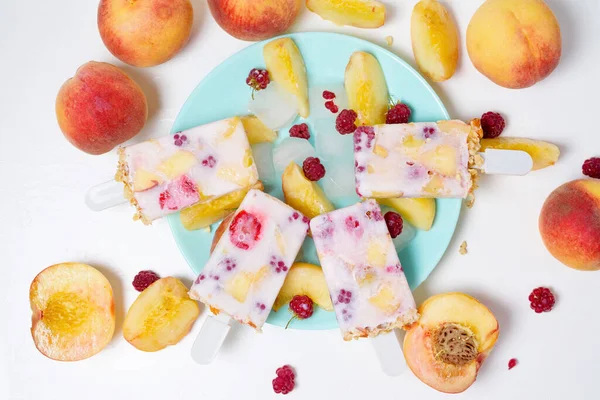 fresh summer ice cream on a stick with peach and raspberry berries . on light background.