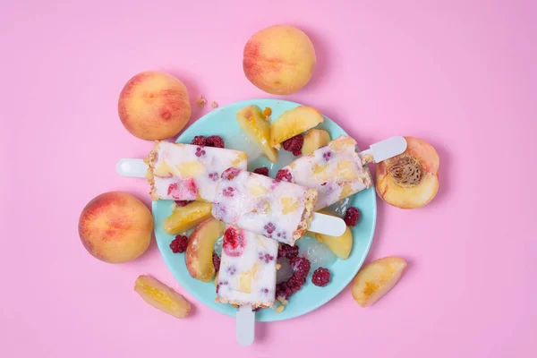 fresh summer ice cream on a stick with peach and raspberry berries on a pink background top view . ice cream ingredients ripe peaches and raspberries with yogurt.