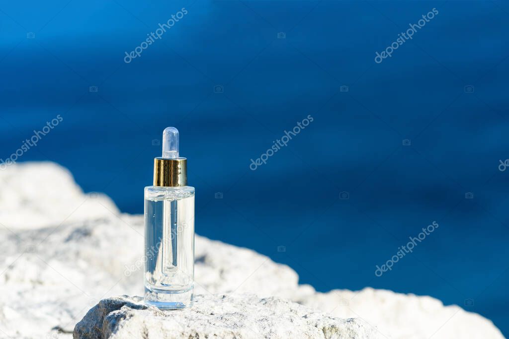 Cosmetic serum in transparent glass dropper bottles on natural stone. Blue sea background, the concept of natural skin care products. Skincare essence for beautiful healthy skin