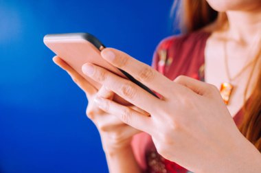 Genç bir kadın mavi arka planda cep telefonu kullanıyor.